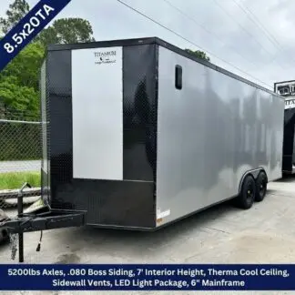 Enclosed dual-axle cargo trailer with a silver exterior and black framing, hitched for towing, factory logo near the front corner.