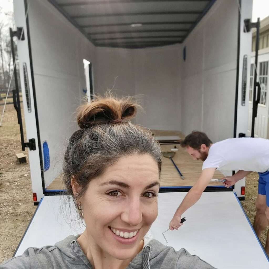 A woman smiles while standing in front of a trailer.