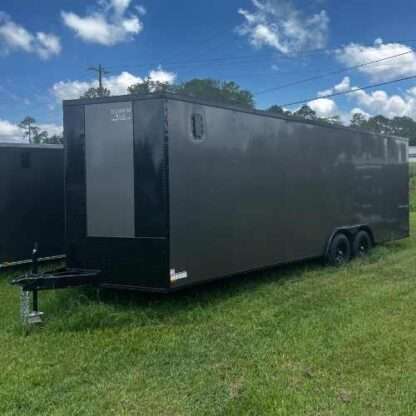 A black trailer parked in the grass near some trees.