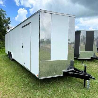 A white trailer parked in the grass near other trailers.