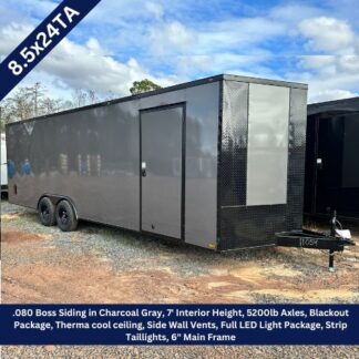 Enclosed gray, dual-axle trailer with a diamond-plate front and a side entry door on a gravel lot.