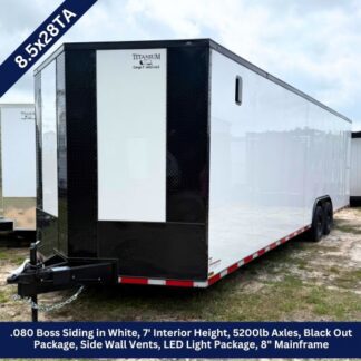 White enclosed cargo trailer with black front panel, tandem axles, and a hitch in a grassy lot.